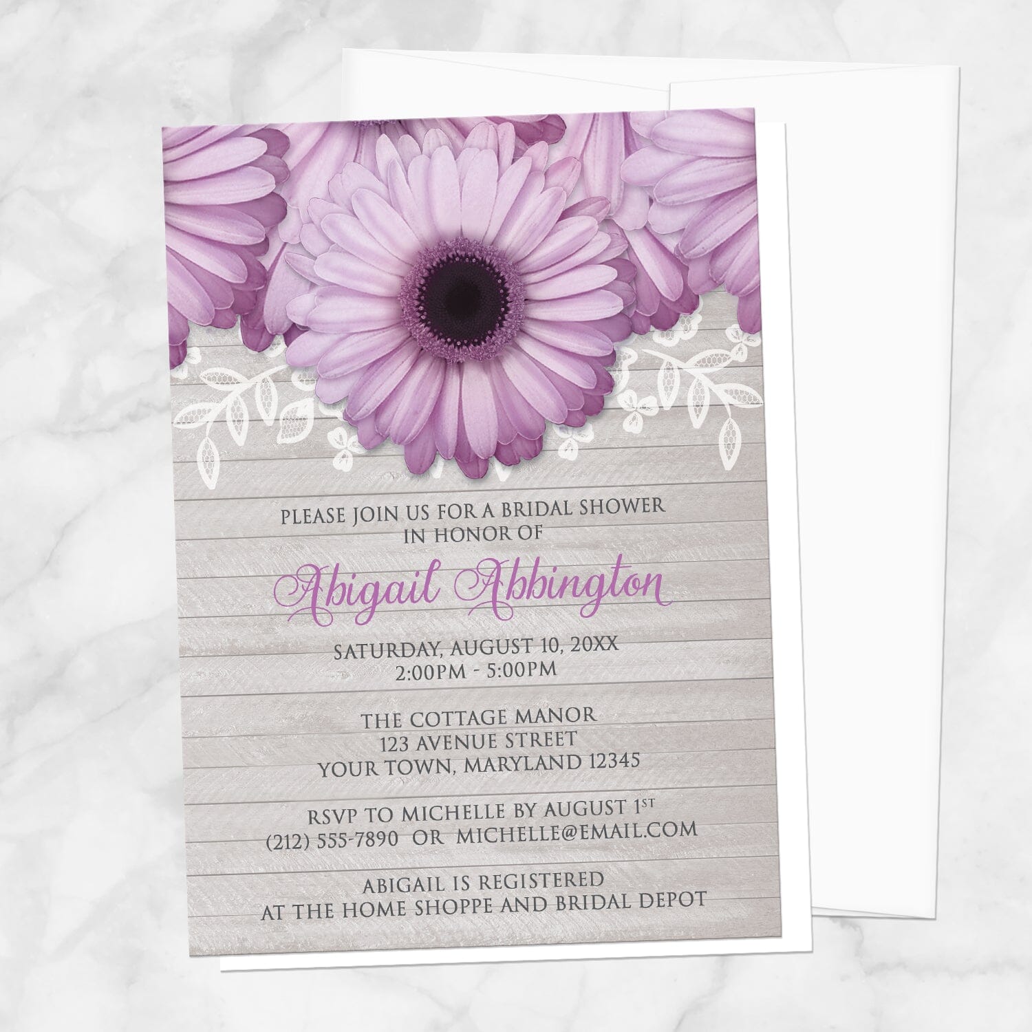 Bridal shower invitation with purple daisies, lace, and gray wood, displayed with a white envelope on a marble surface
