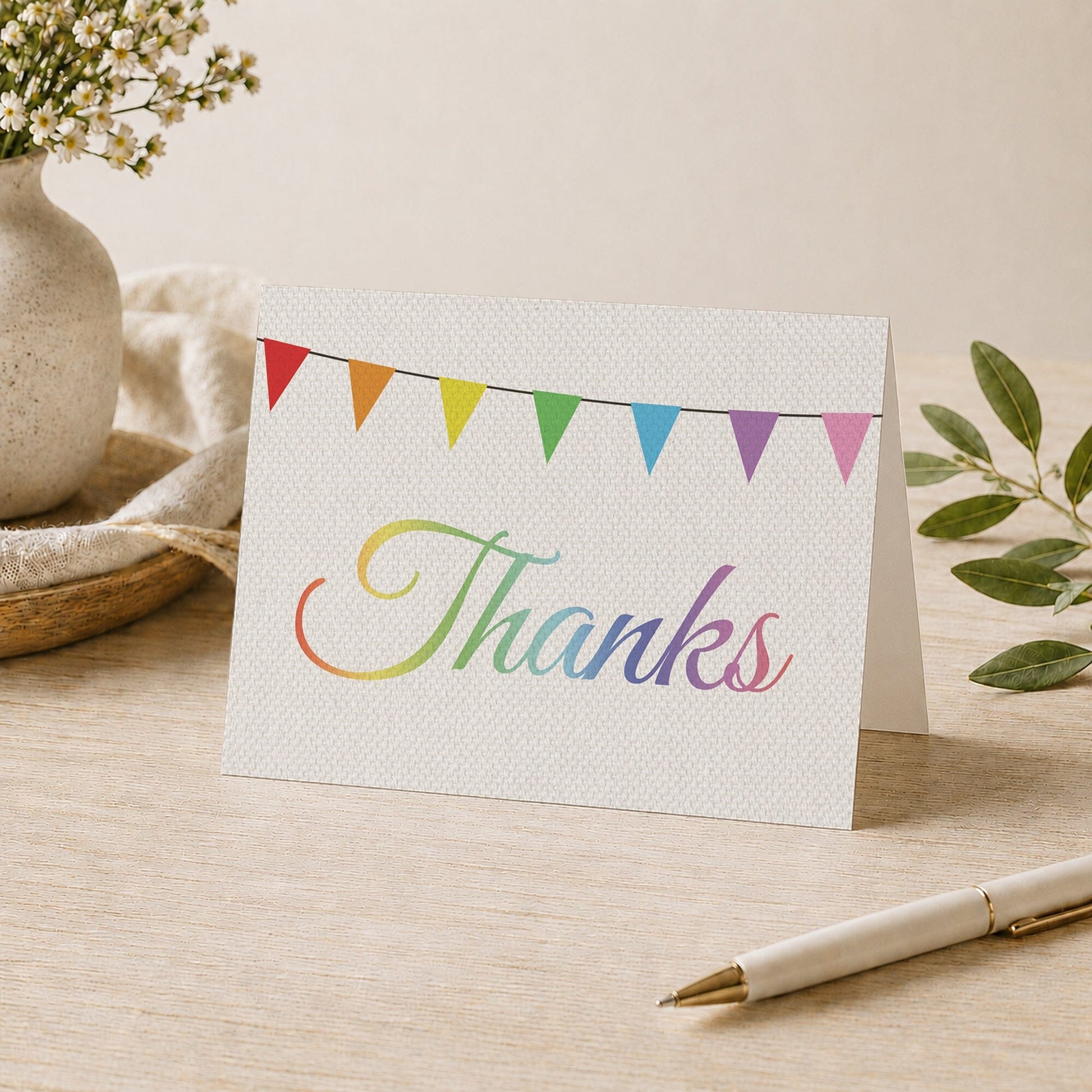 Rustic Rainbow Bunting Flags Thank You Card shown on a desk with a vase, plants, and a pen.