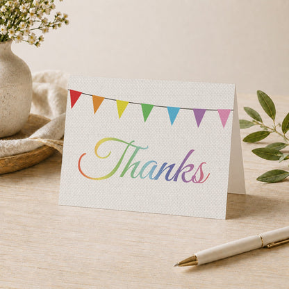Rustic Rainbow Bunting Flags Thank You Card shown on a desk with a vase, plants, and a pen.
