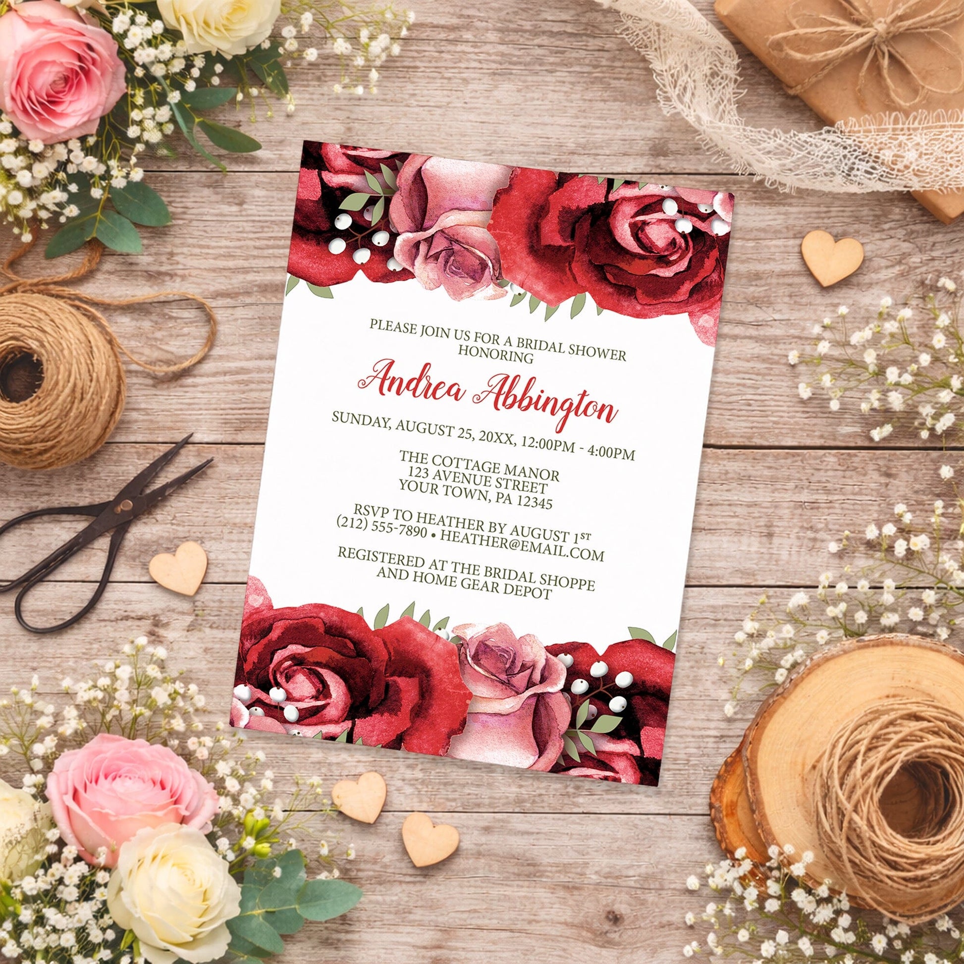 Bridal shower invitation with red and pink roses on a wooden surface with spring and summer flowers, small wood hearts, and twine.
