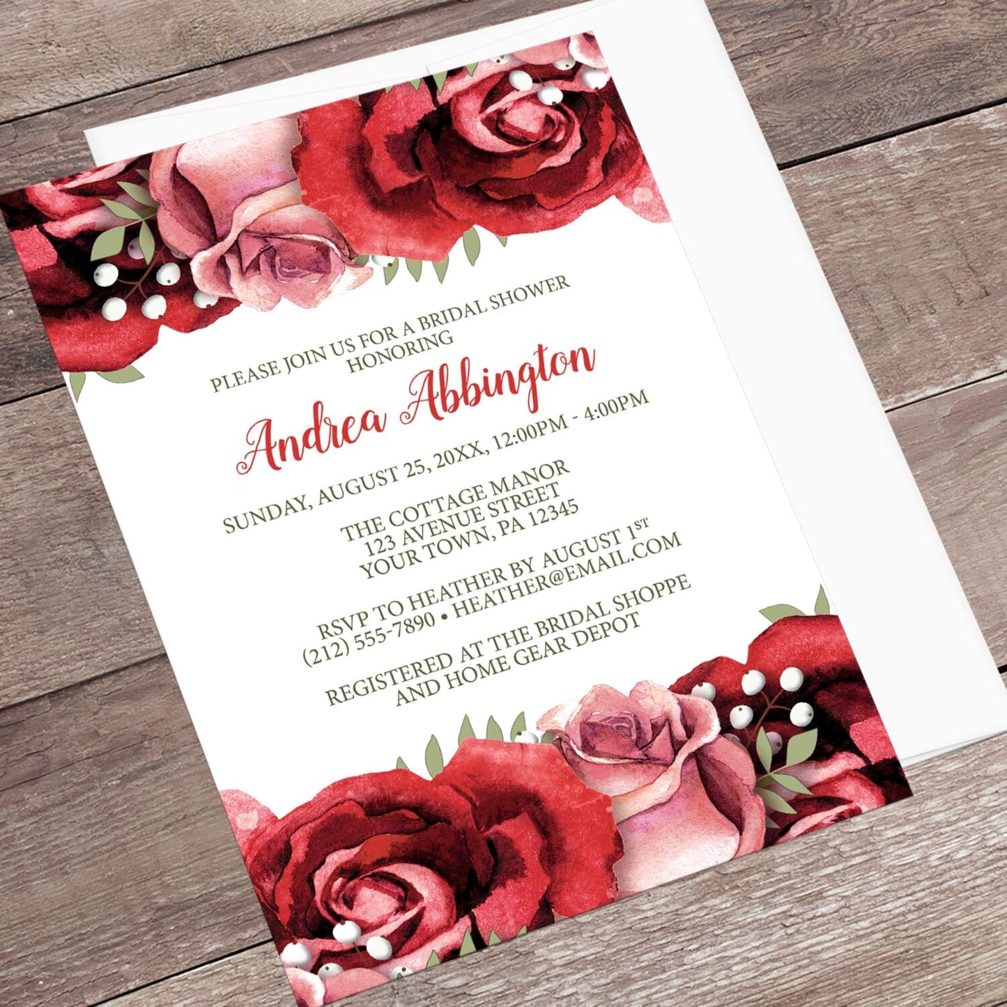 Rustic Red Pink Rose Green White Bridal Shower Invitation shown at an angle on a wooden surface with a white envelope.