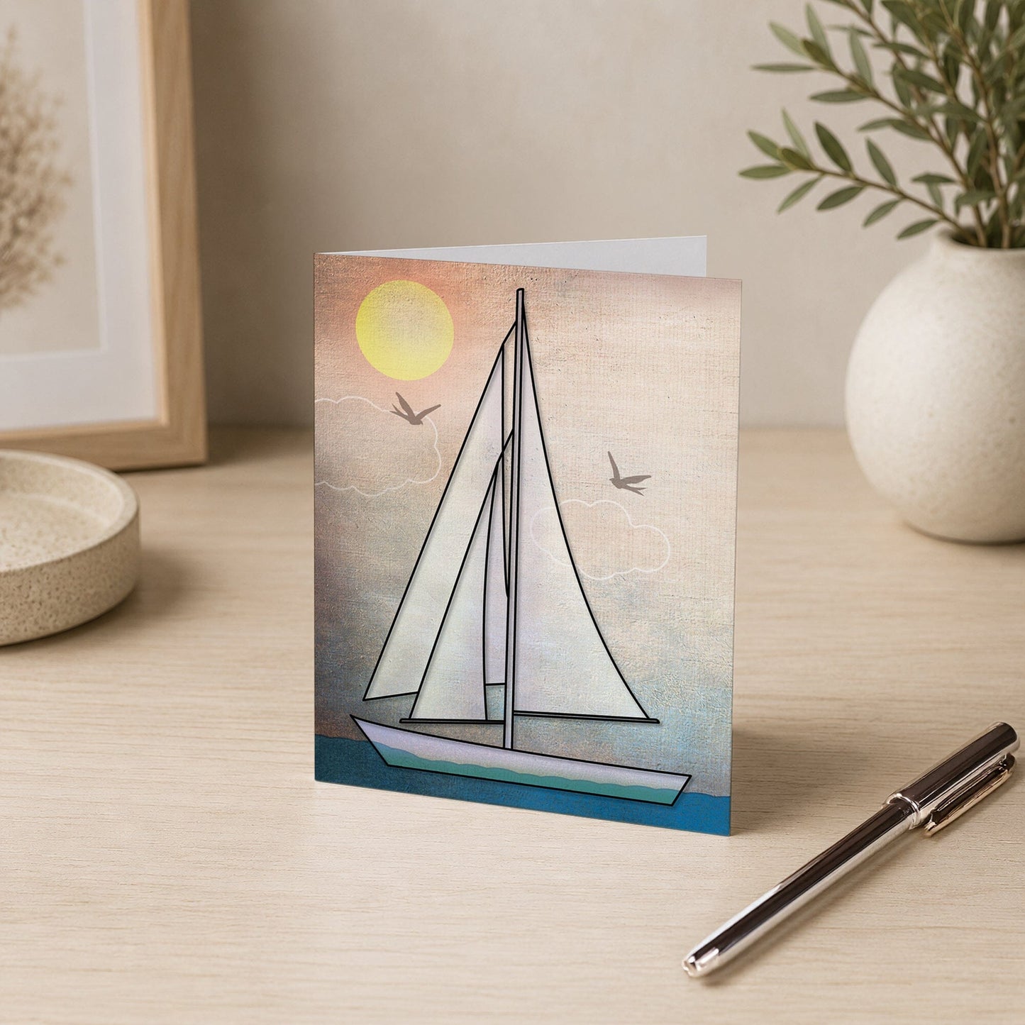 Rustic Sailboat Nautical Note Card shown on a desk with a vase and a pen.