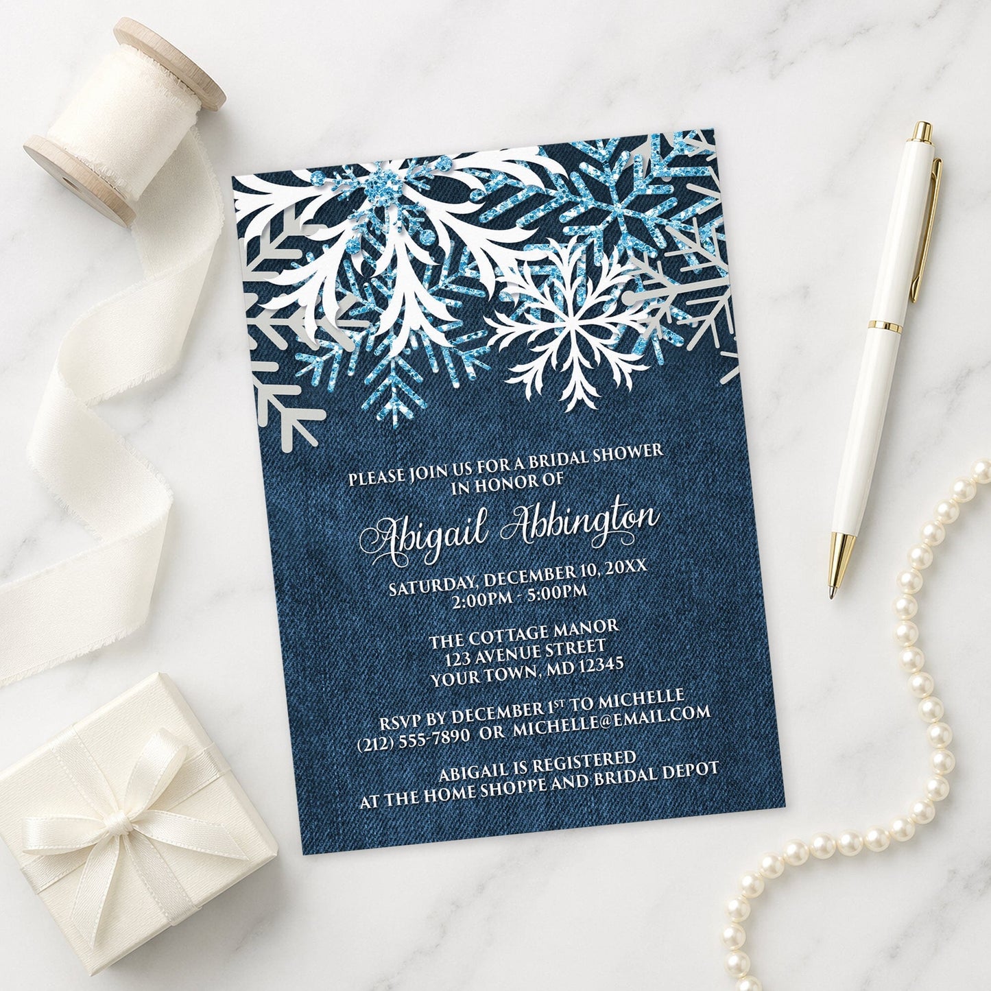 Rustic Snowflake Denim Winter Bridal Shower Invitation shown on a marble surface with a white gift box, pen, ribbon, and pearls.