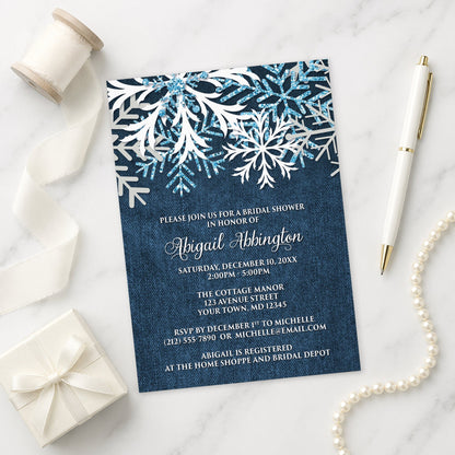 Rustic Snowflake Denim Winter Bridal Shower Invitation shown on a marble surface with a white gift box, pen, ribbon, and pearls.