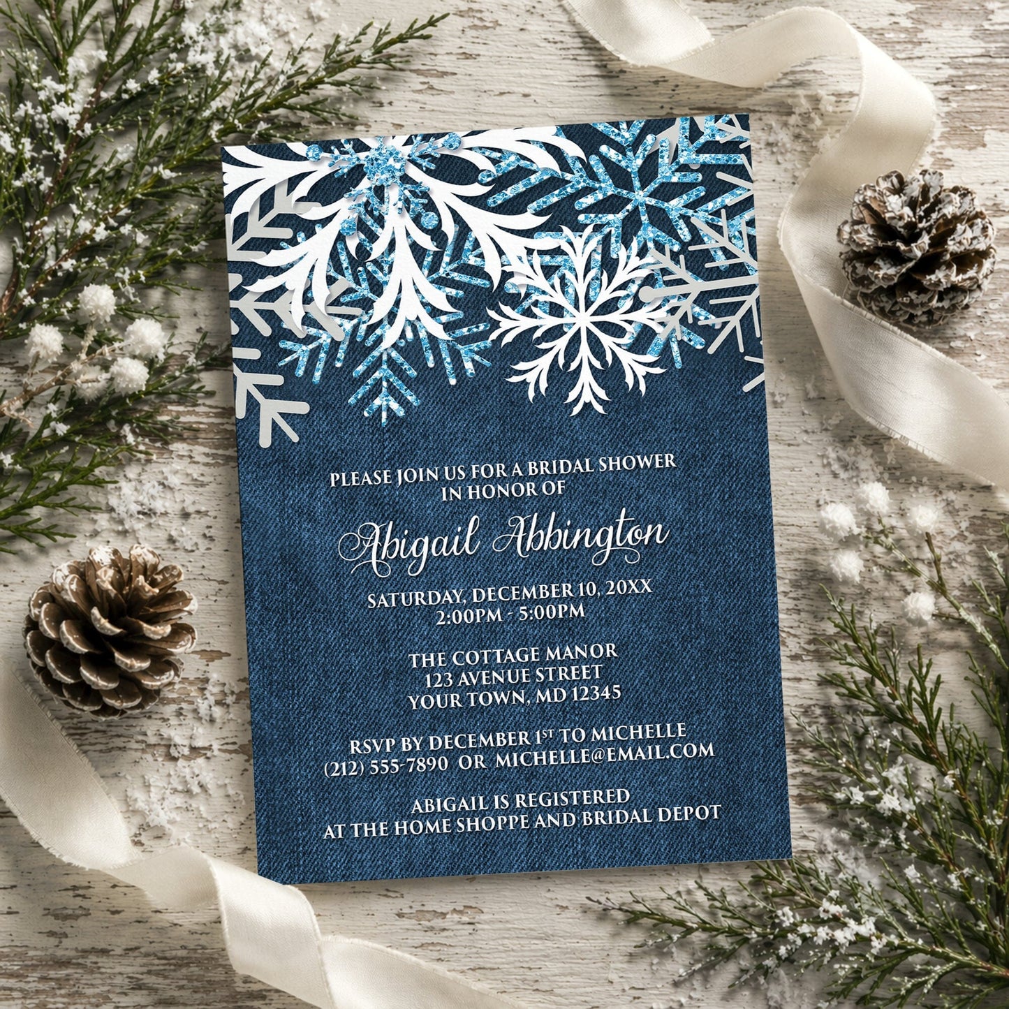 Rustic Snowflake Denim Winter Bridal Shower Invitation shown on a painted wood background with winter greenery, pine cones, and ribbons.