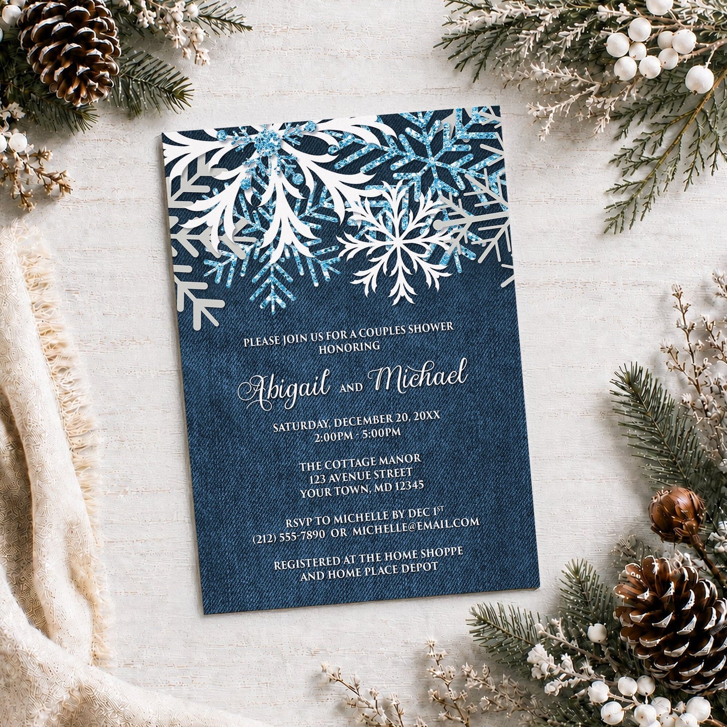 Rustic Snowflake Denim Winter Couples Shower Invitation on a light surface with winter greenery, a blanket, and pine cones.