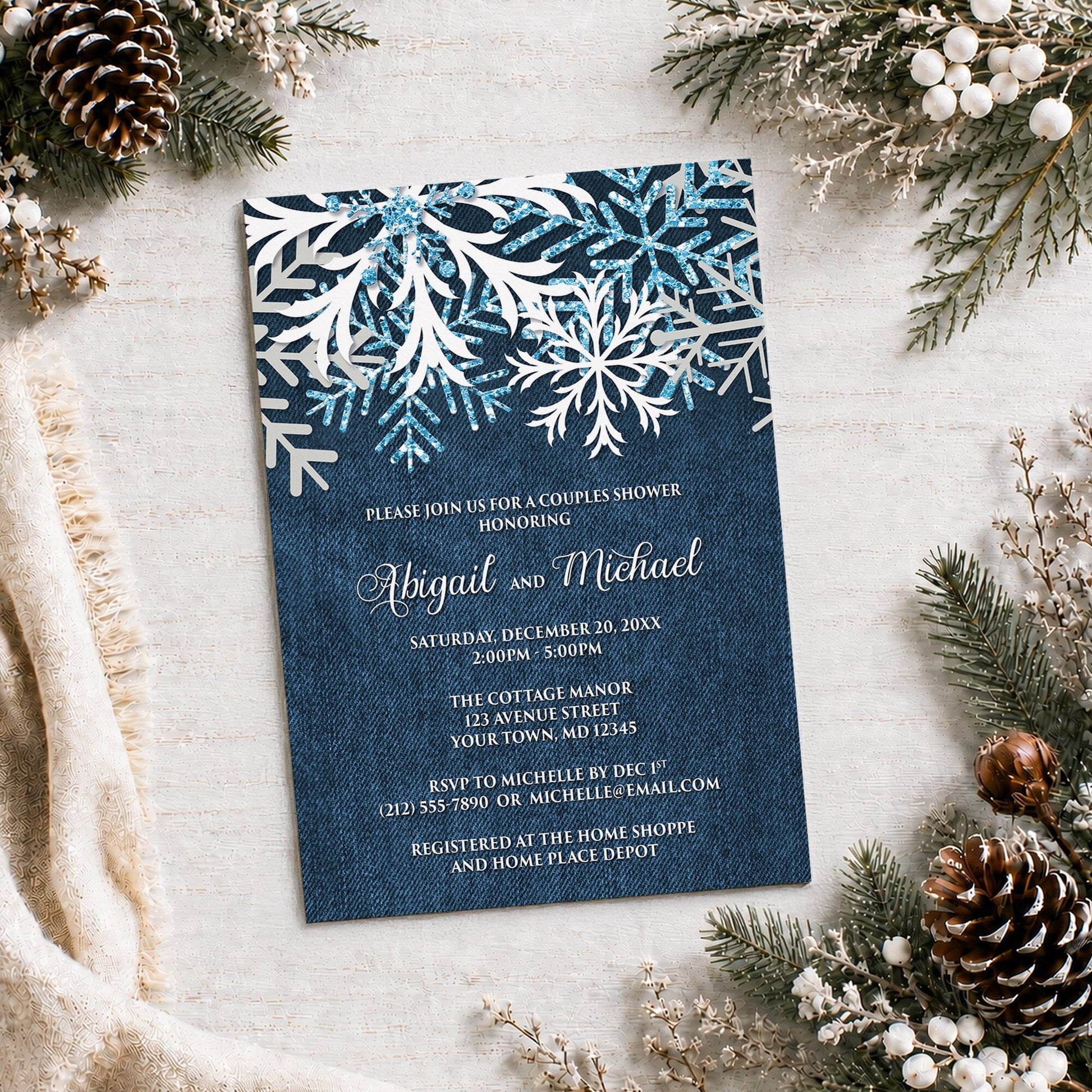 Rustic Snowflake Denim Winter Couples Shower Invitation on a light surface with winter greenery, a blanket, and pine cones.