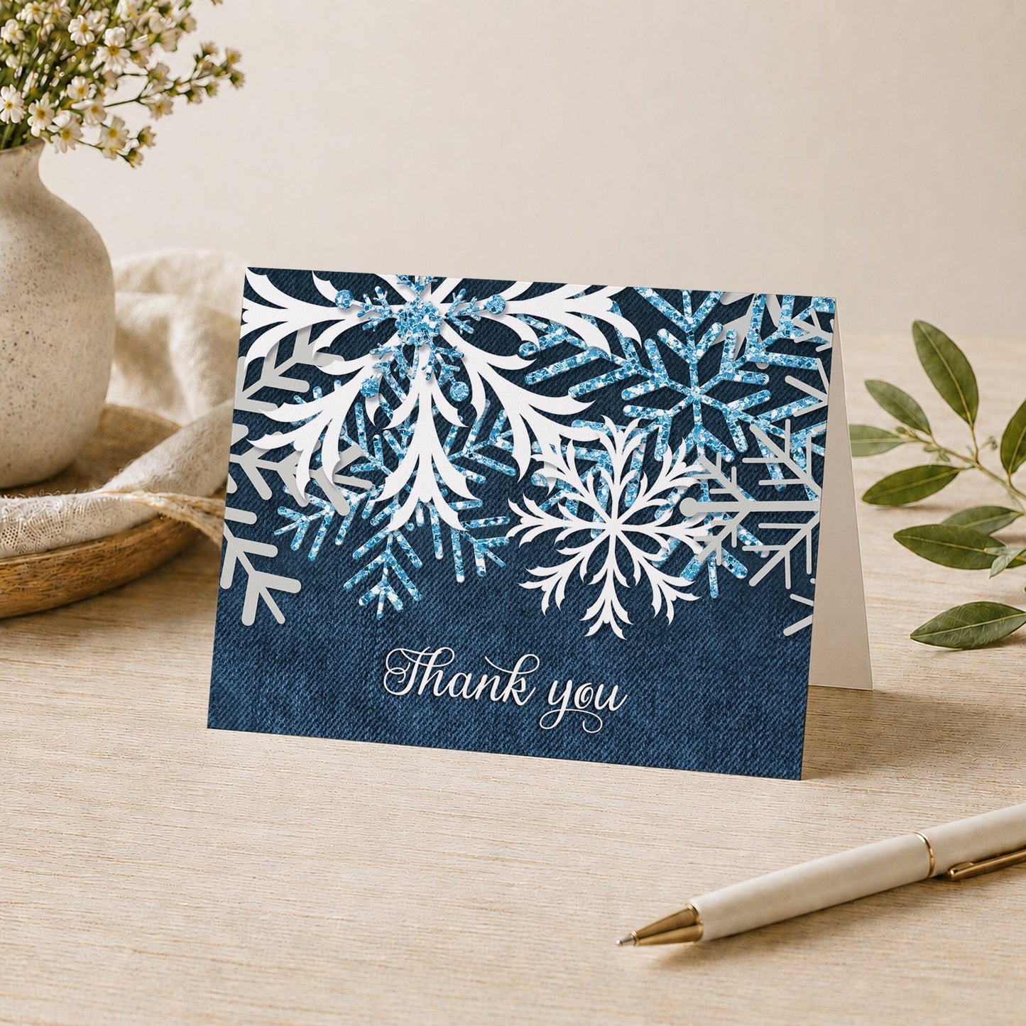 Rustic Snowflake Denim Winter Thank You Card shown on a desk with a vase, plants, and a pen.