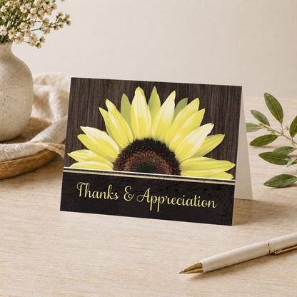 Rustic Sunflower Black Thank You Card shown on a desk with a vase, plants, and a pen.