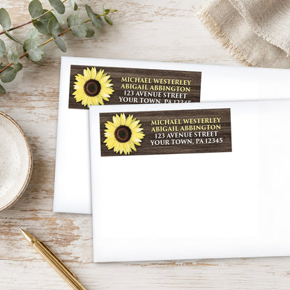 Address labels with a sunflower design with rustic brown wood, on white envelopes, shown on a wooden surface with eucalyptus leaves and a pen.