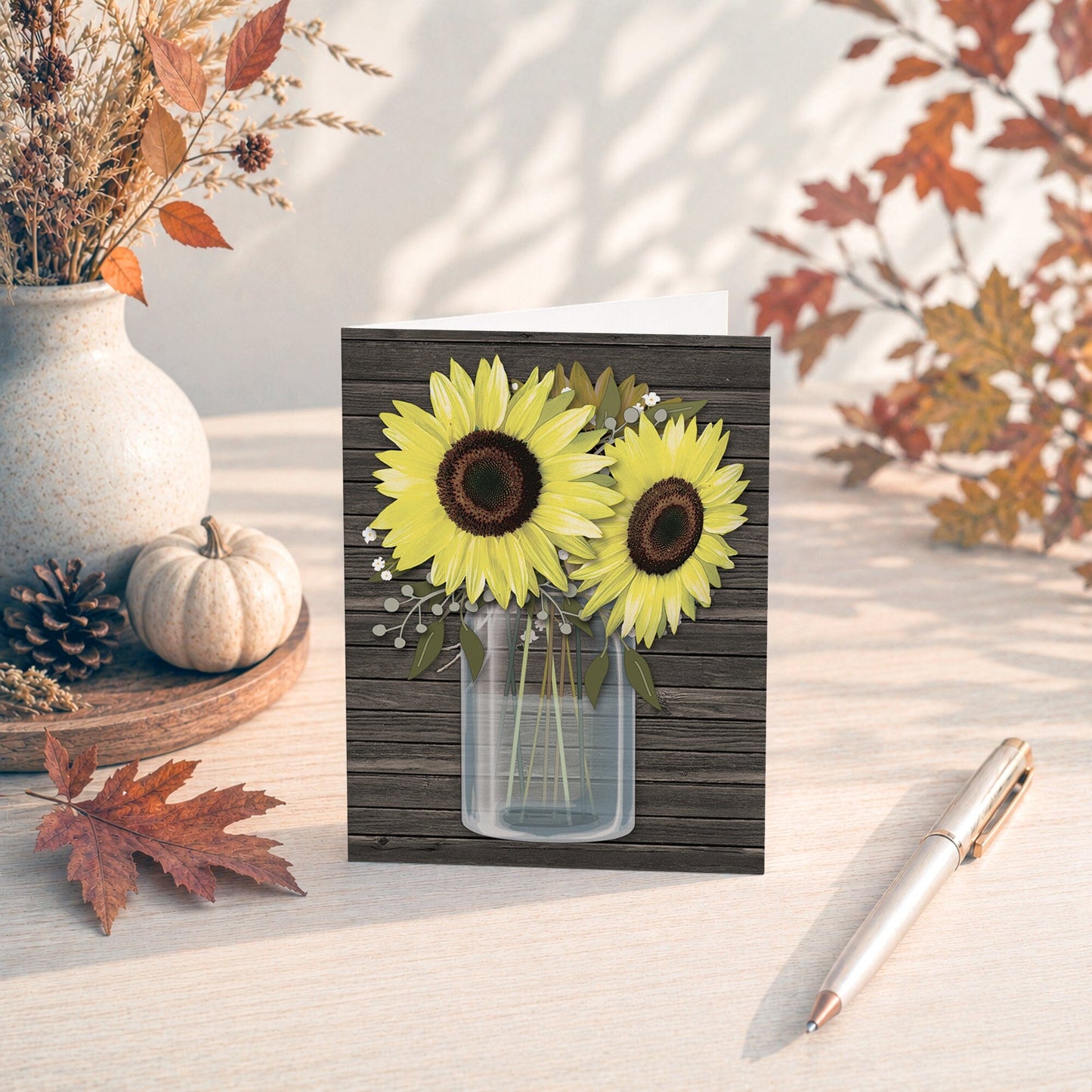 Rustic Sunflower Wood Mason Jar Note Card shown on a tabletop with a fall leaves, autumn decor, and a pen.