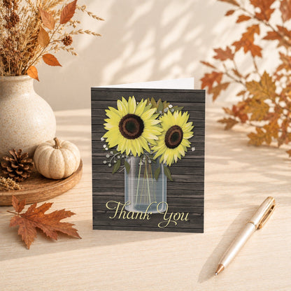 Rustic Sunflower Wood Mason Jar Thank You Card shown on a tabletop with fall leaves, autumn decor, and a pen.