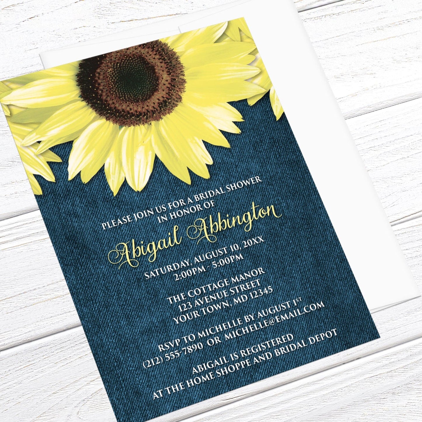 Bridal Shower invitation with large yellow sunflowers and blue denim, displayed at an angle with a white envelope on a white wood surface