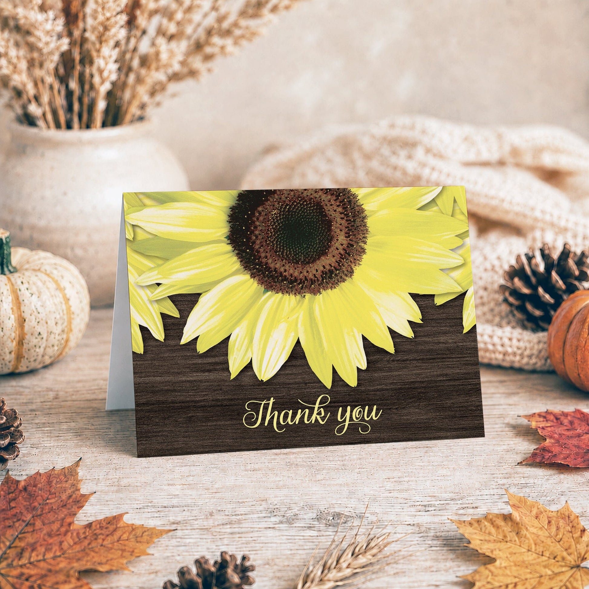 Rustic Sunflower and Wood Thank You Card shown on a tabletop with a vase, autumn decor, and a pine cone.