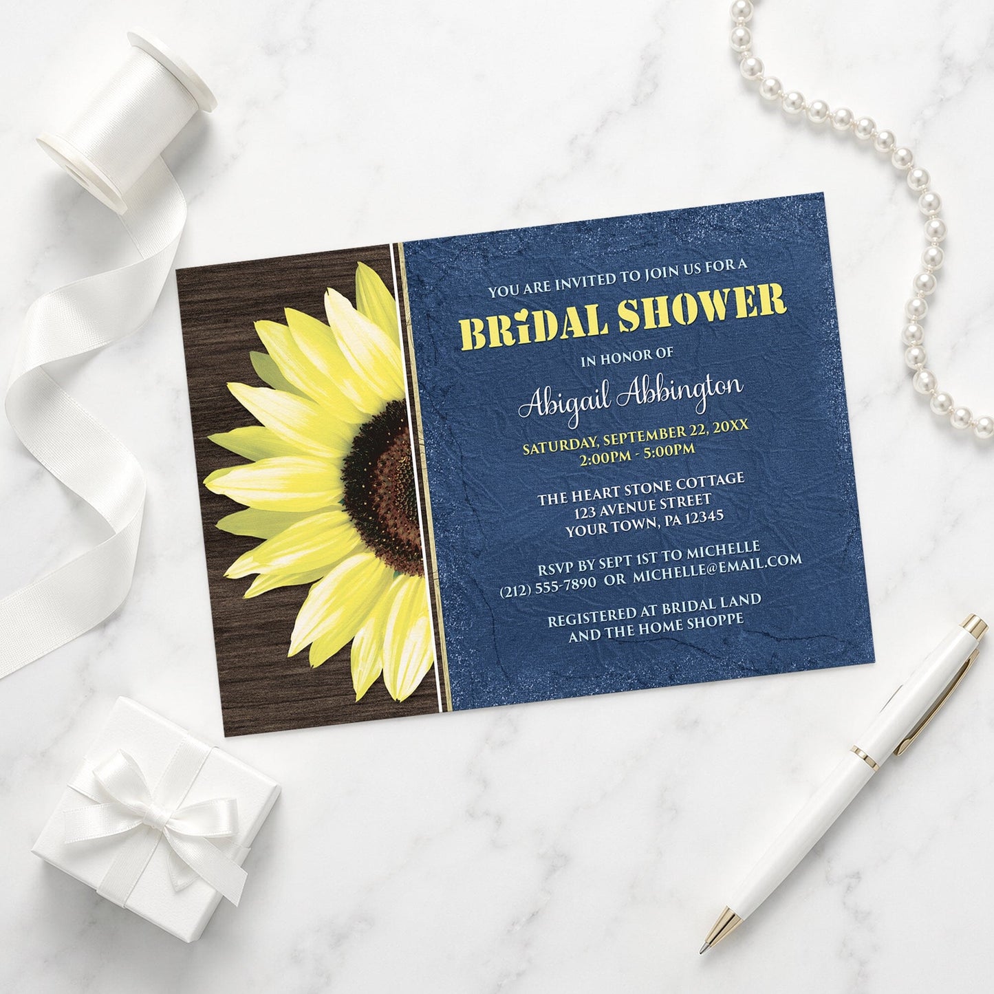 Rustic Sunflower with Blue Bridal Shower Invitation shown on a marble surface with a white gift box, pen, ribbon, and pearls.
