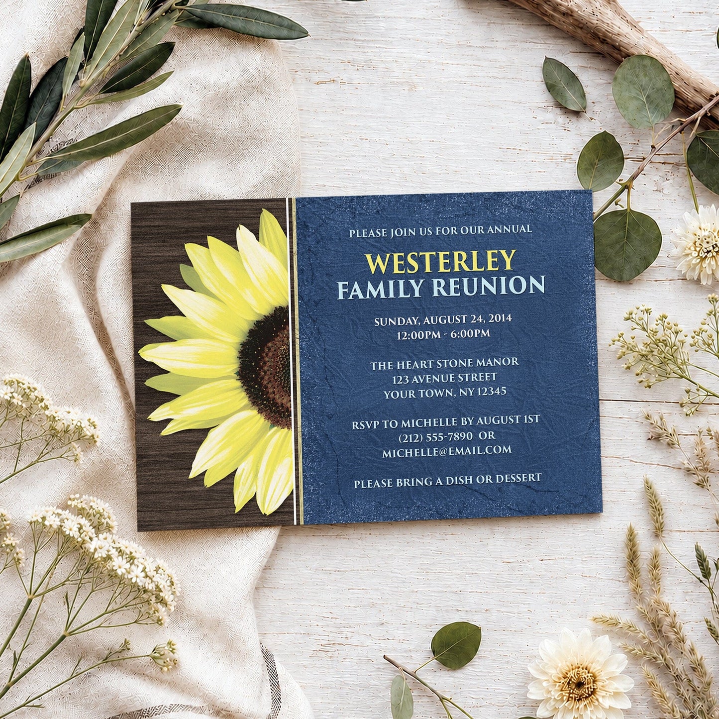 Rustic Sunflower with Blue Family Reunion Invitation shown on a light wooded surface with spring and summer plants.