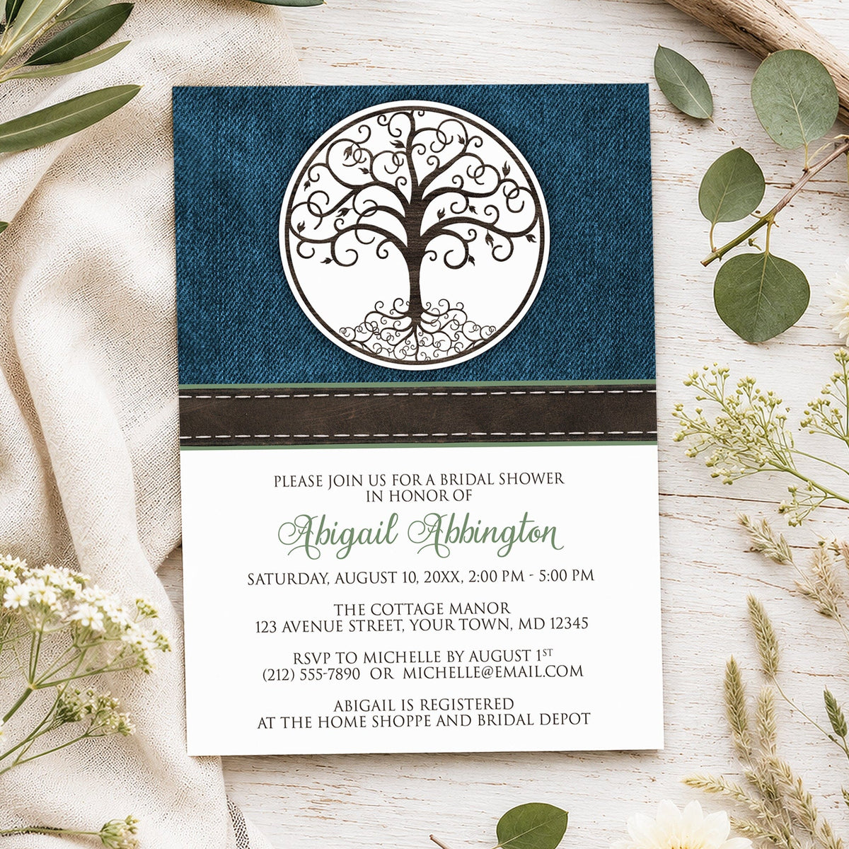 Rustic Tree of Life bridal shower invitation with brown decorative tree-of-life design, blue denim background, brown stitched ribbon, and green personalized name, styled on a light wood surface with linen fabric and spring and summer-inspired greenery.