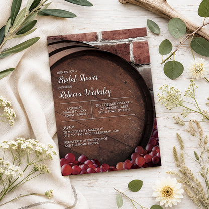 Rustic Wine Barrel Vineyard Bridal Shower Invitation shown on a light wooden surface with spring and summer plants.