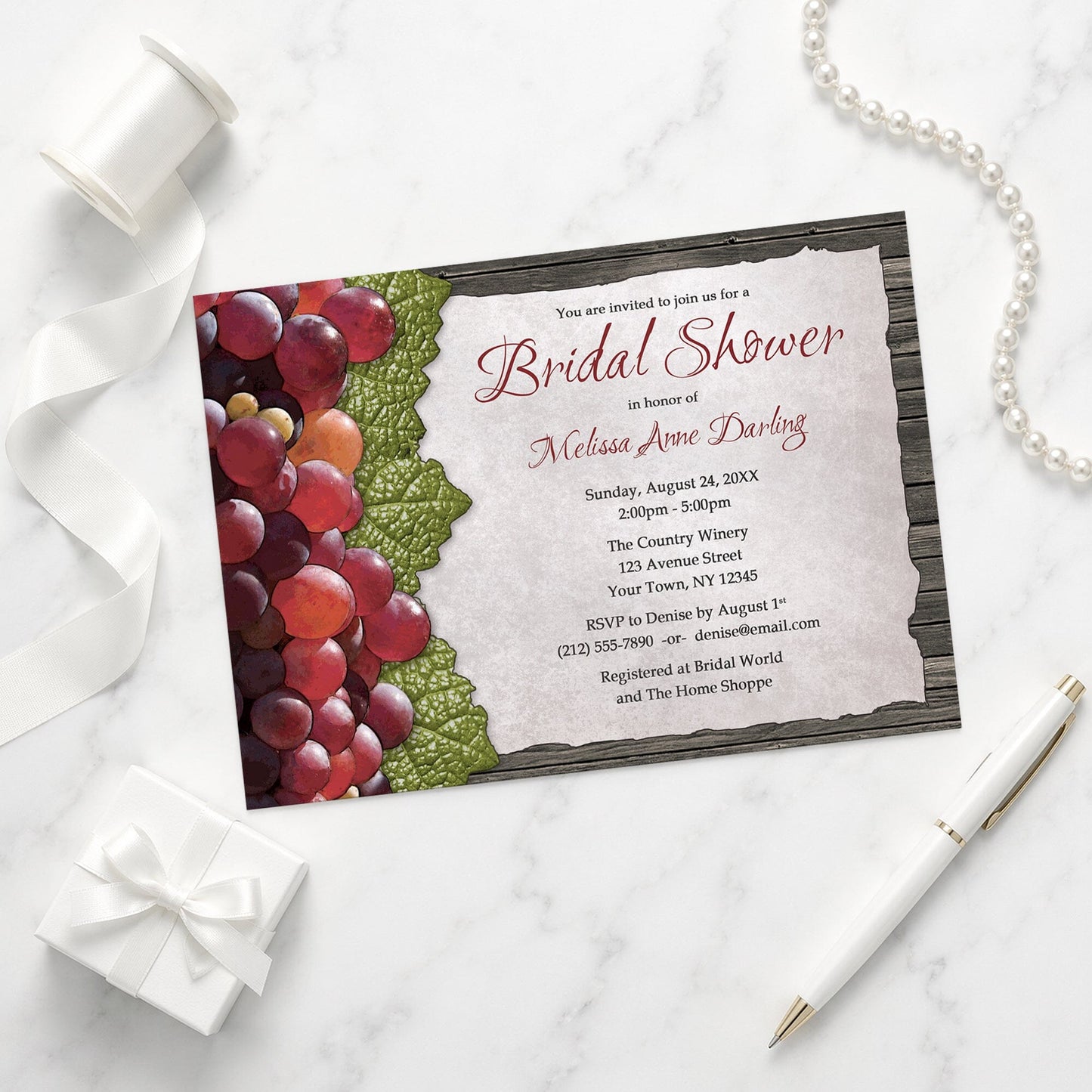 Rustic Winery Grapes and Wood Bridal Shower Invitation shown on a marble surface with a white gift box, pen, ribbon, and pearls.