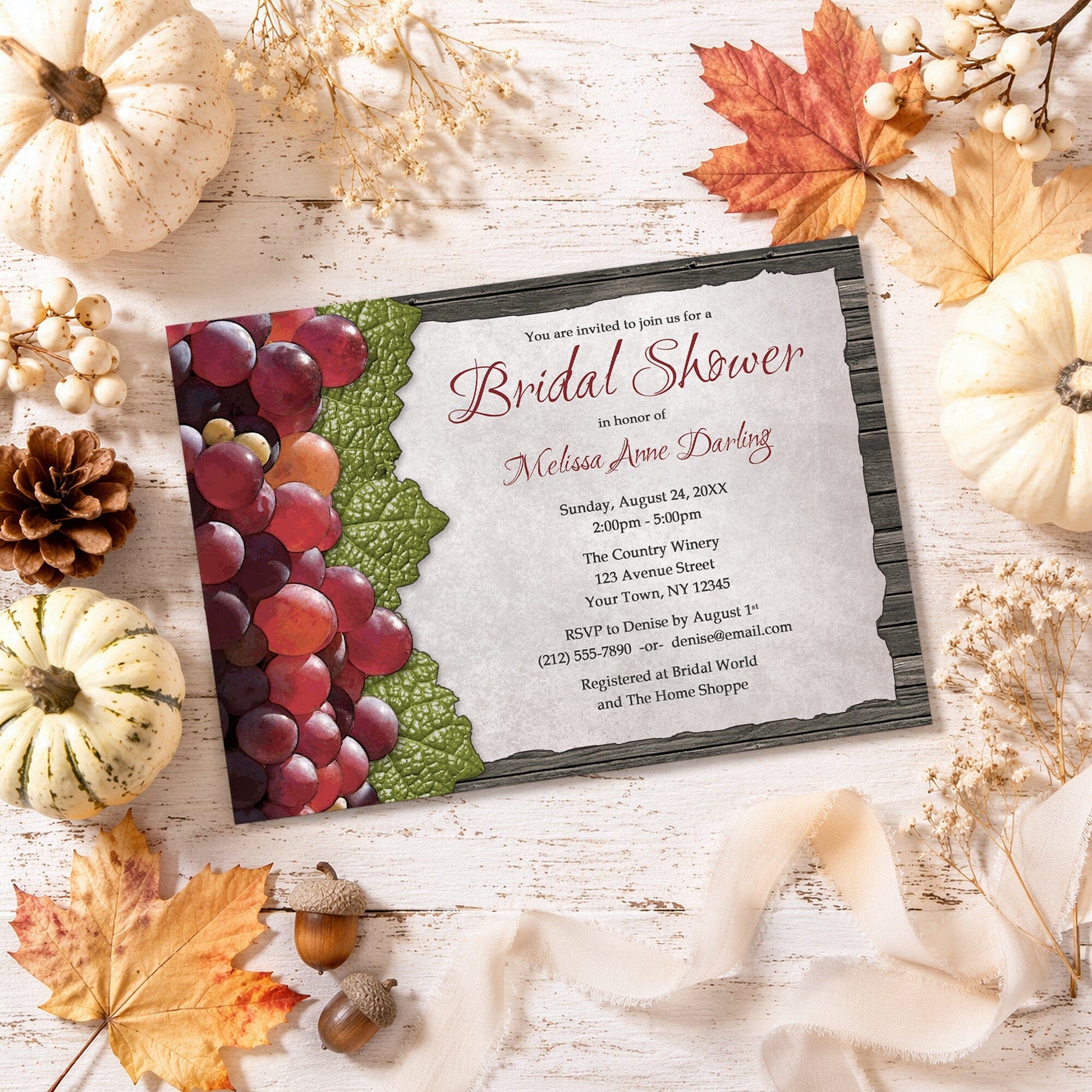 Rustic Winery Grapes and Wood Bridal Shower Invitation shown on a painted wooden surface with fall leaves and autumn decor.