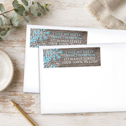 Rustic Winter Wood Blue Snowflake Address Labels, shown on white envelopes, on a wooden surface with eucalyptus leaves and a pen.