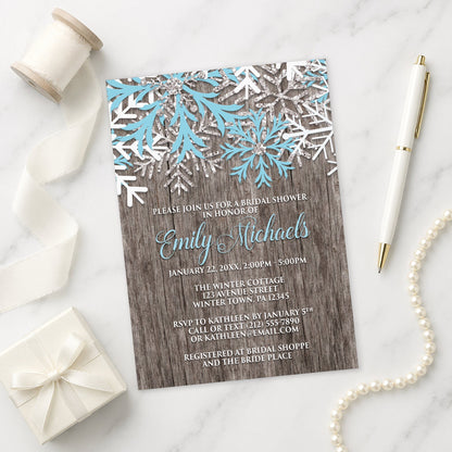 Rustic Winter Wood Blue Snowflake Bridal Shower Invitation shown on a marble surface with a white gift box, pen, ribbon, and pearls.