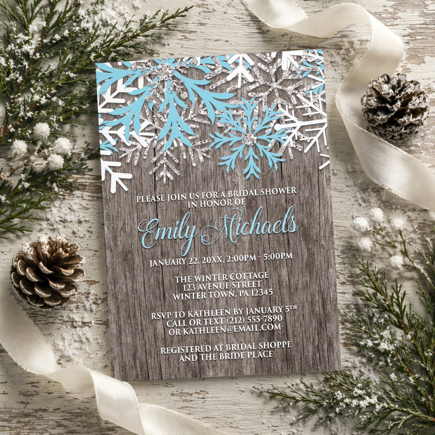 Rustic Winter Wood Blue Snowflake Bridal Shower Invitation shown on a rustic surface with winter greenery, pine cones, and ribbons.