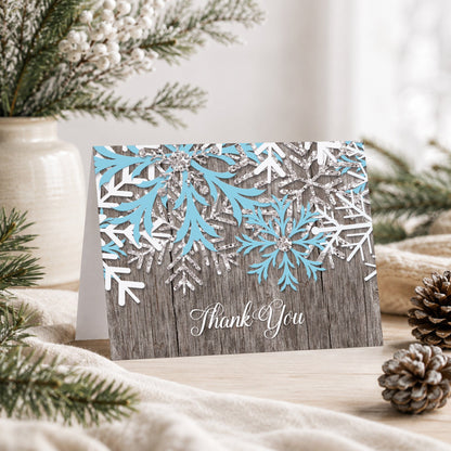 Rustic Winter Wood Blue Snowflake Thank You Card shown on a tabletop with a vase, winter greenery, and pine cones.