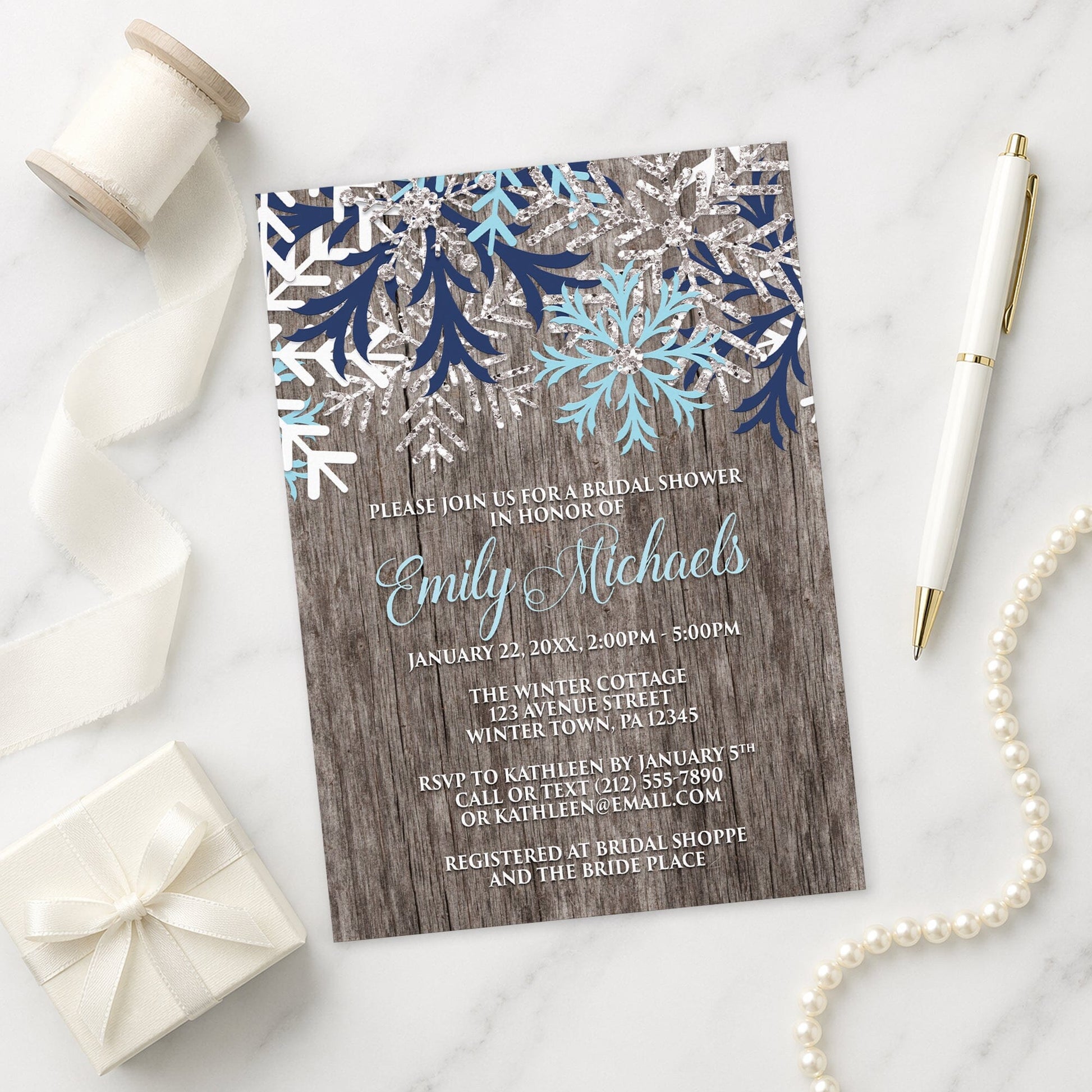 Rustic Winter Wood Navy Aqua Snowflake Bridal Shower Invitation shown on a marble surface with a white gift box, pen, ribbon, and pearls.
