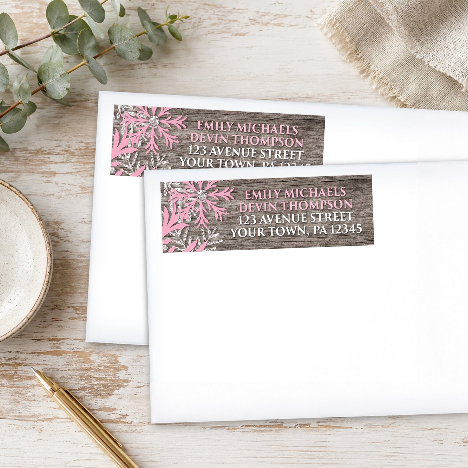 Rustic Winter Wood Pink Snowflake Address Labels, shown on white envelopes, on a wooden surface with a pen and eucalyptus leaves.