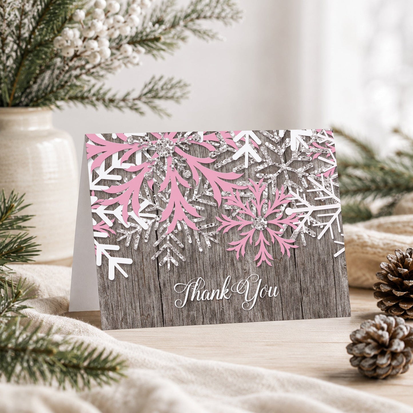 Rustic Winter Wood Pink Snowflake Thank You Card shown on a tabletop with a vase, winter greenery, and pine cones.