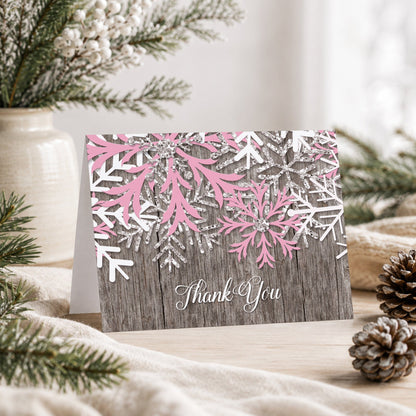 Rustic Winter Wood Pink Snowflake Thank You Card shown on a tabletop with a vase, winter greenery, and pine cones.
