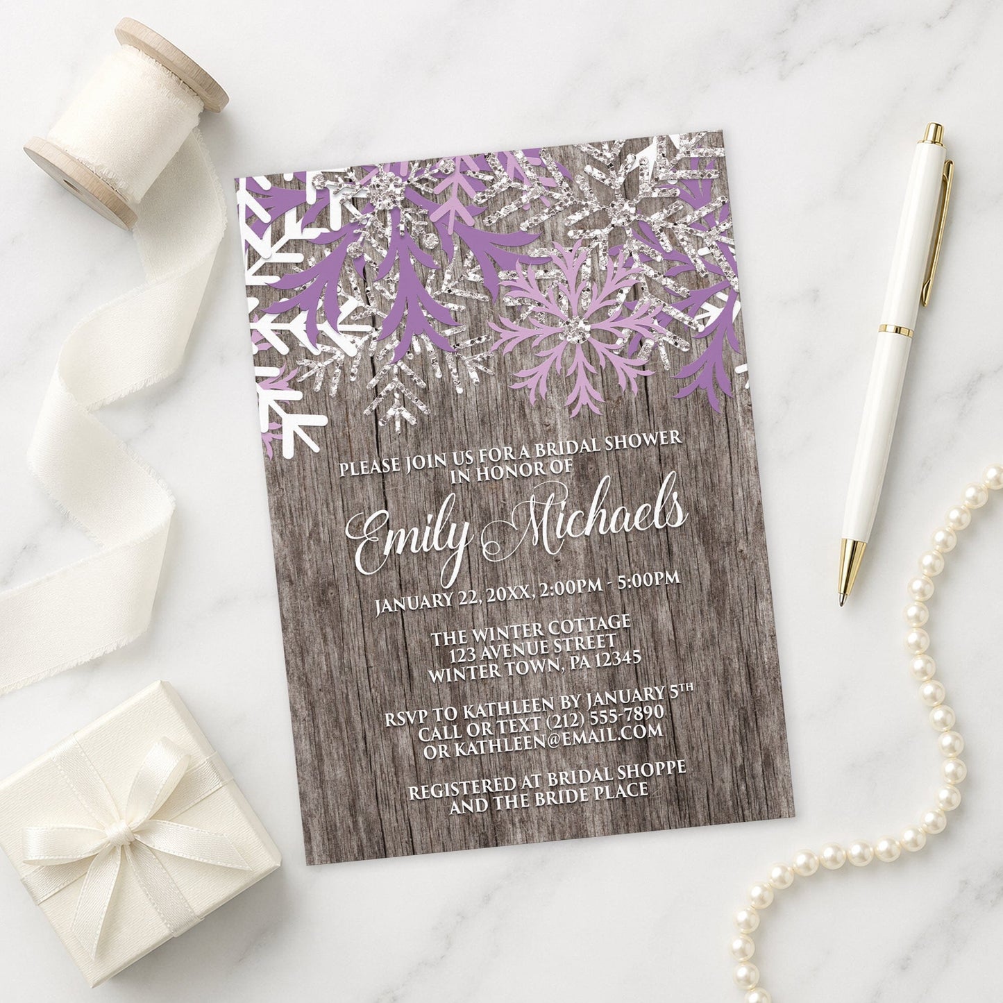 Rustic Winter Wood Purple Snowflake Bridal Shower Invitation on a marble surface with decorative items.