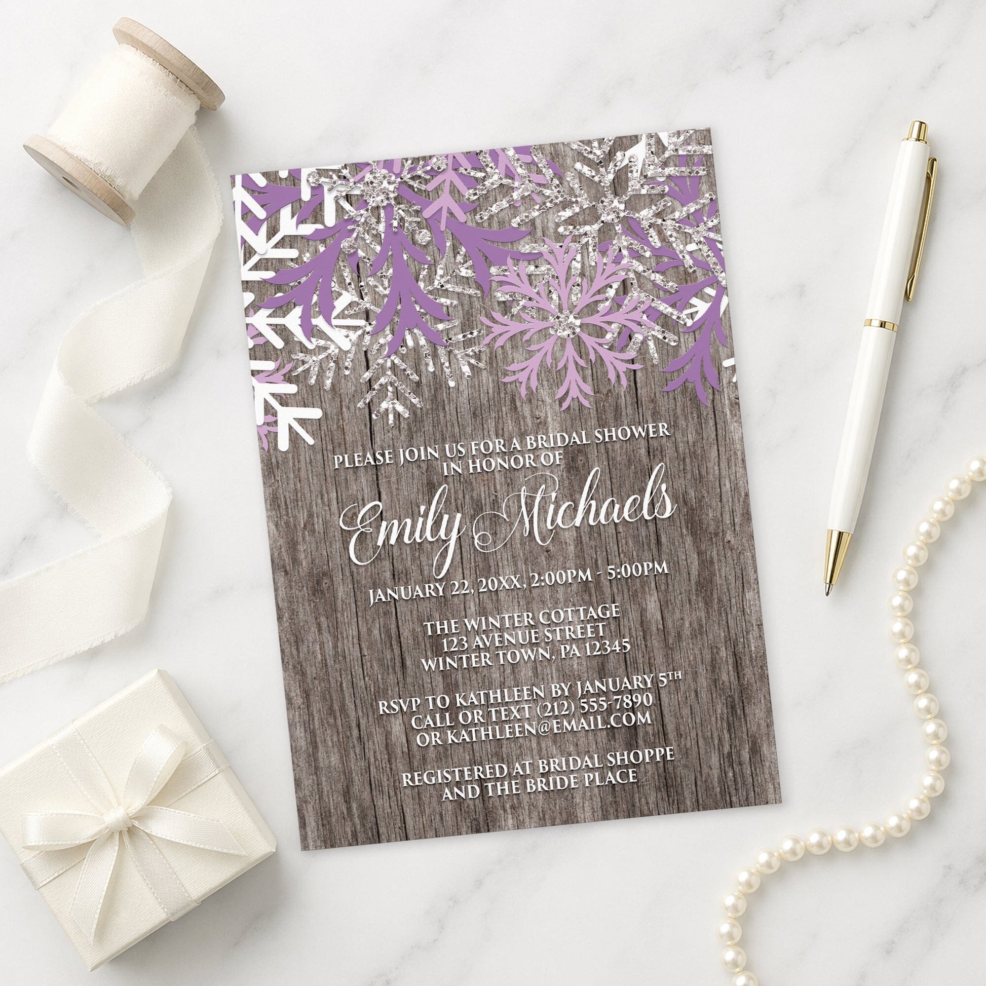 Rustic Winter Wood Purple Snowflake Bridal Shower Invitation on a marble surface with decorative items.