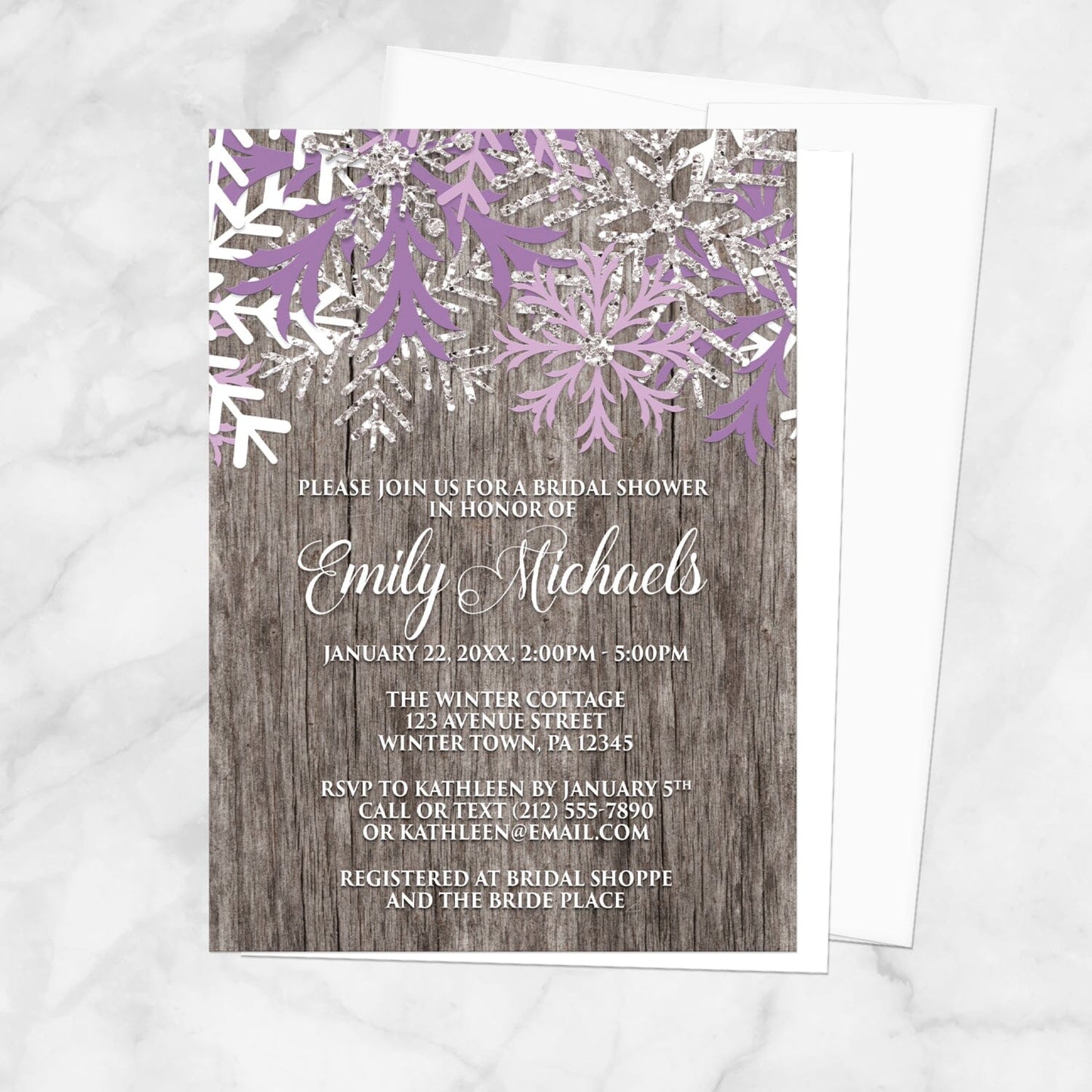 Bridal shower invitation with purple snowflakes on a wooden background, displayed with a white envelope on a marble surface