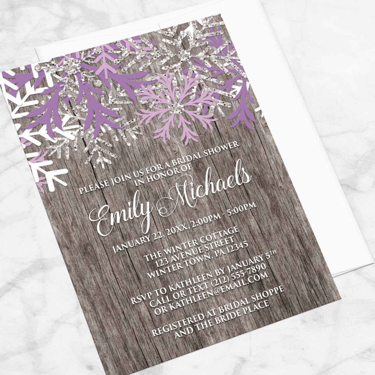 Bridal shower invitation with purple snowflakes on a wooden background, displayed at an angle with a white envelope on a marble surface