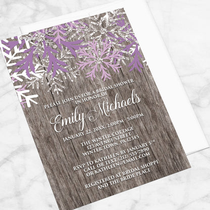 Bridal shower invitation with purple snowflakes on a wooden background, displayed at an angle with a white envelope on a marble surface