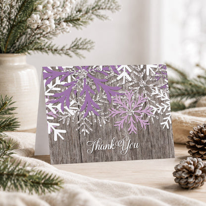 Rustic Winter Wood Purple Snowflake Thank You Card shown on a tabletop with a vase, winter greenery, and pine cones.