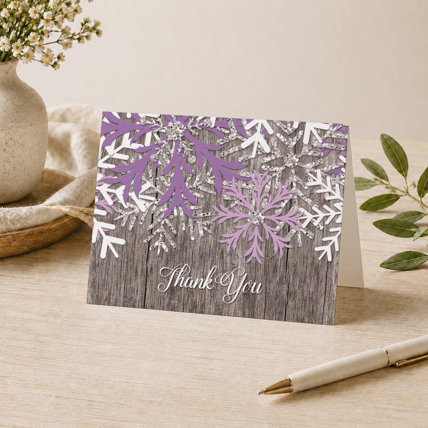 Rustic Winter Wood Purple Snowflake Thank You Card shown on a desk with a vase, plants, and a pen.