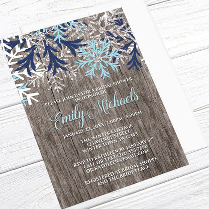 Rustic Winter Wood Navy Aqua Snowflake Bridal Shower Invitation shown at an angle on a light wood surface with a white envelope.