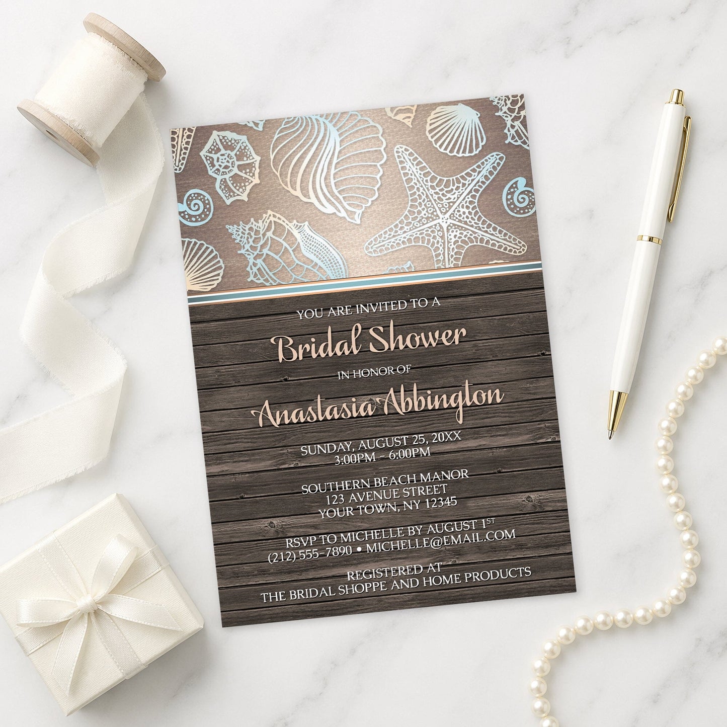 Rustic Wood Beach Seashell Bridal Shower Invitation shown on a marble surface with a white gift box, pen, ribbon, and pearls.