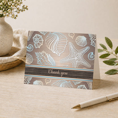 Rustic Wood Beach Seashell Thank You Card shown on a desk with a vase, plants, and a pen.