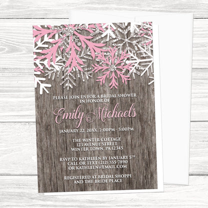 Rustic Winter Wood Pink Snowflake Bridal Shower Invitation shown on a light wood surface with a white envelope.