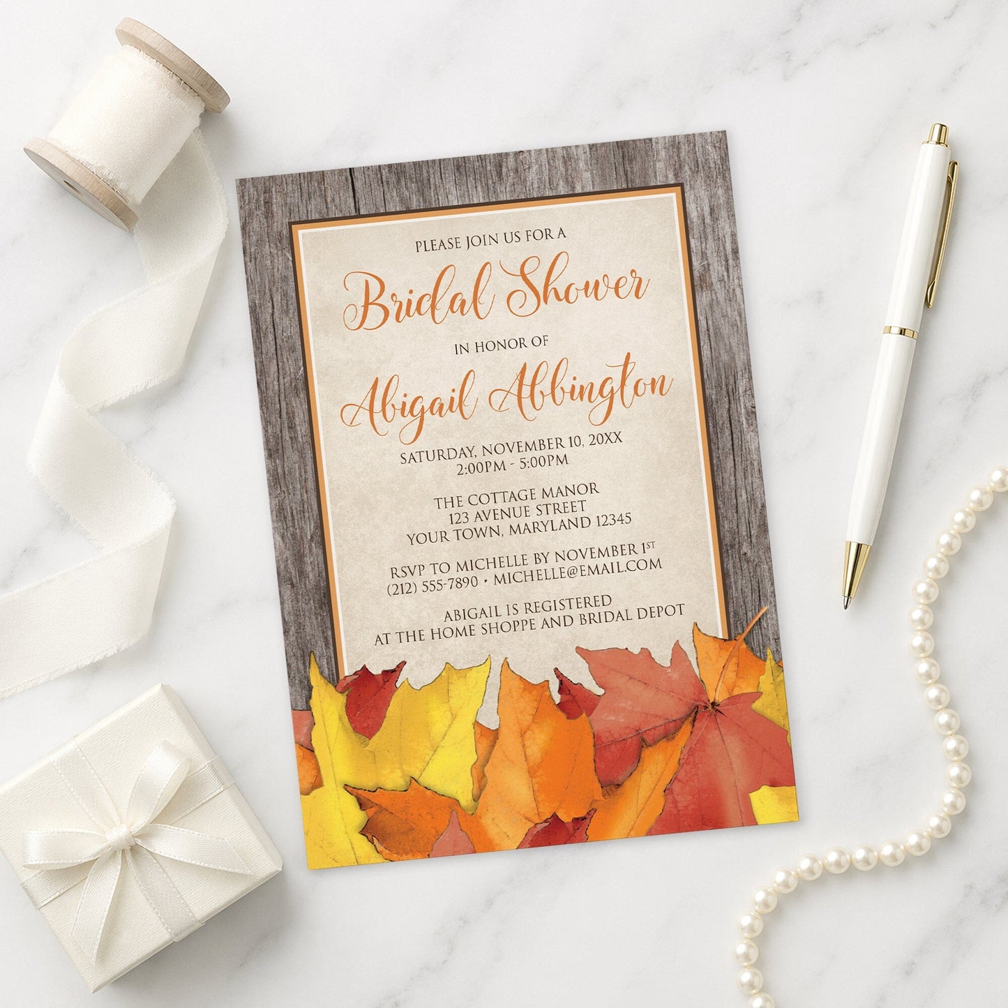 Rustic Wood and Leaves Fall Bridal Shower Invitation shown on a marble surface with a white gift box, pen, ribbon, and pearls.