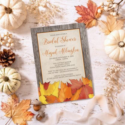 Rustic Wood and Leaves Fall Bridal Shower Invitation shown on a painted wooden surface with fall leaves and autumn decor.