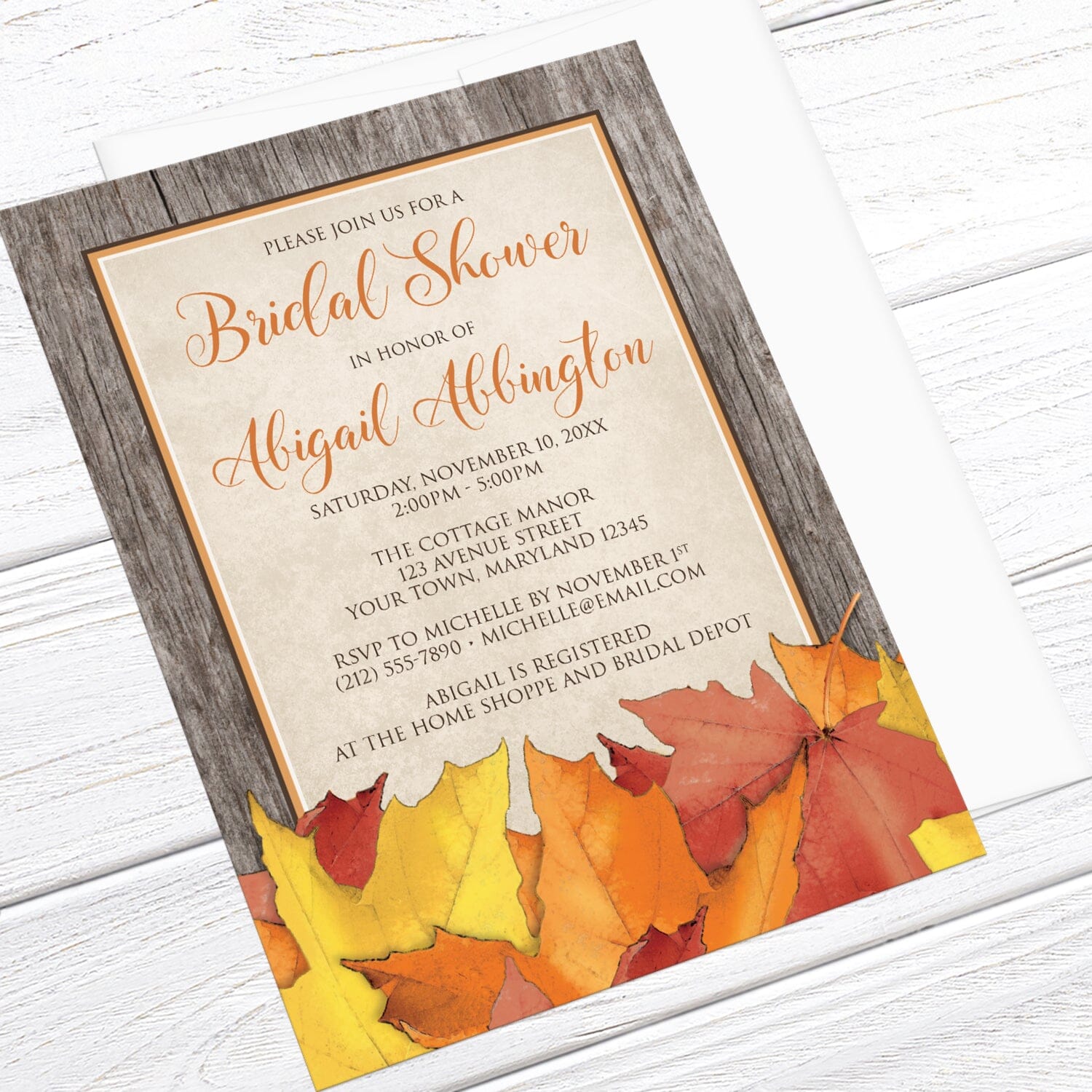 Rustic Wood and Leaves Fall Bridal Shower Invitation shown at an angle on a light wood surface with a white envelope.