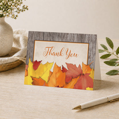 Rustic Wood and Leaves Fall Thank You Card on a desk with a vase and a pen.