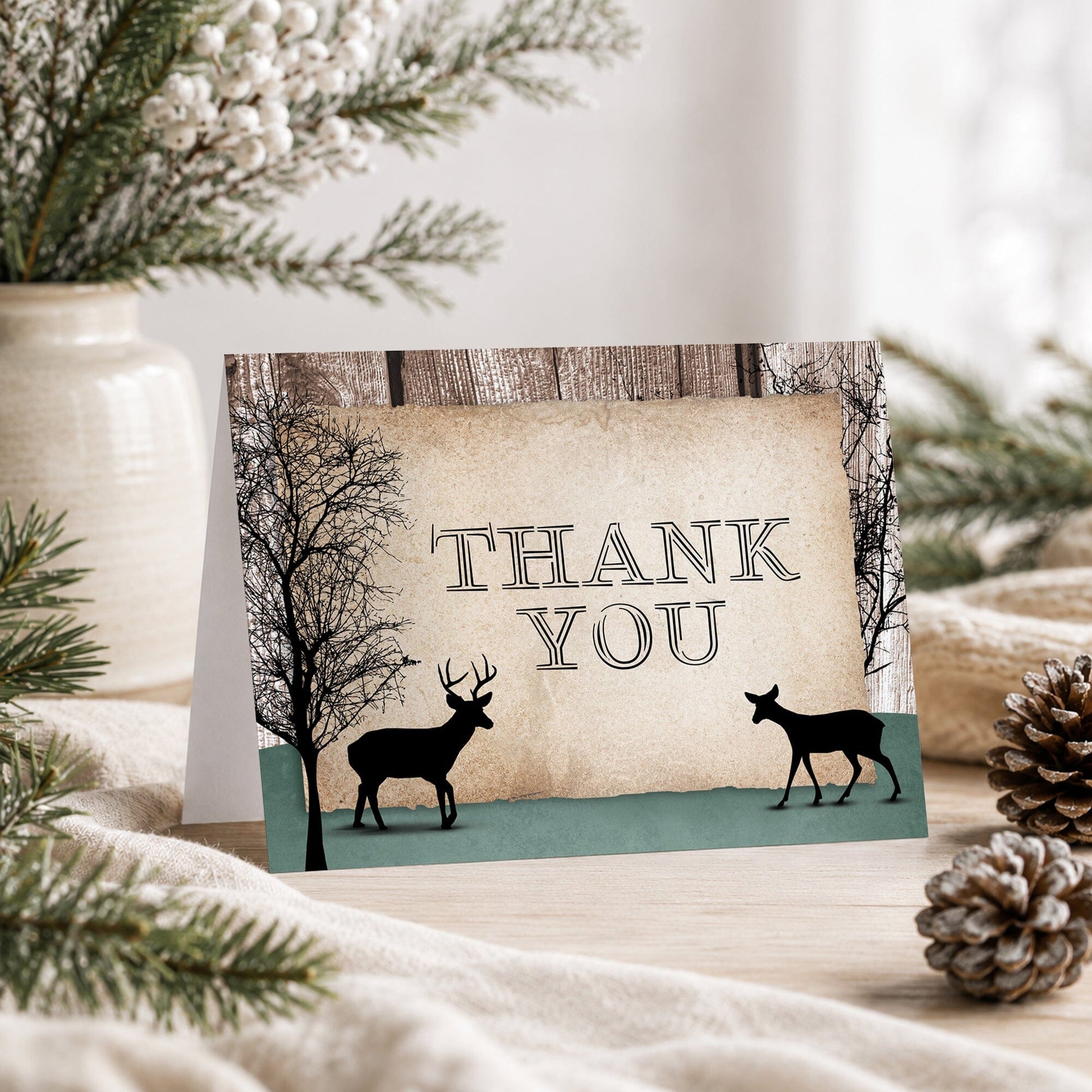 Rustic Woodsy Deer Thank You Card shown on a tabletop with winter greenery, a vase, and pine cones.