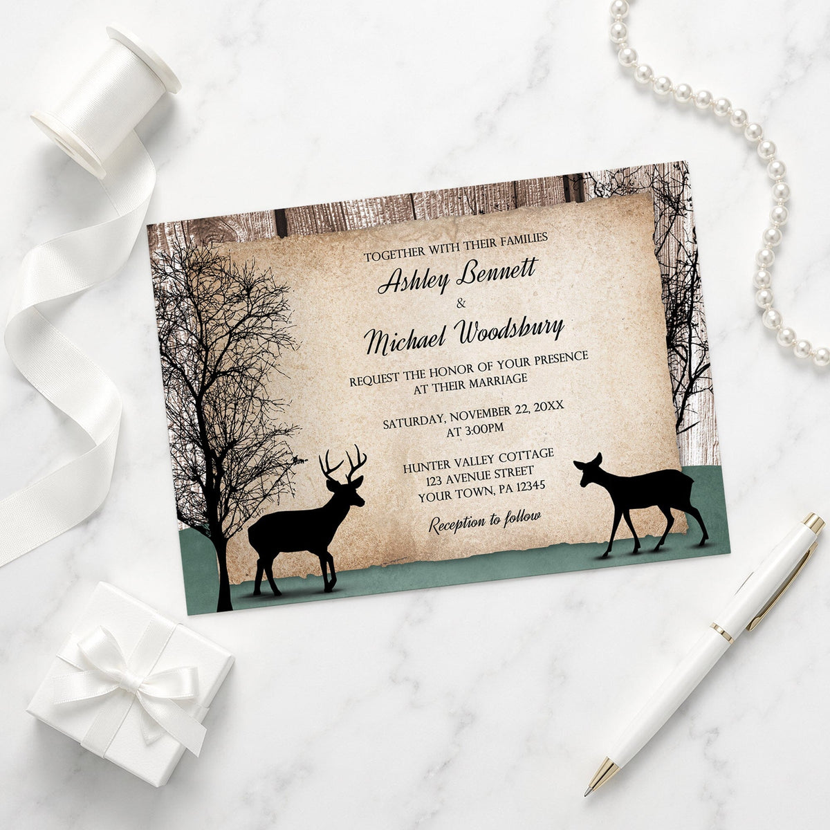 Rustic wedding invitation with deer design on a marble surface with ribbon and pen.