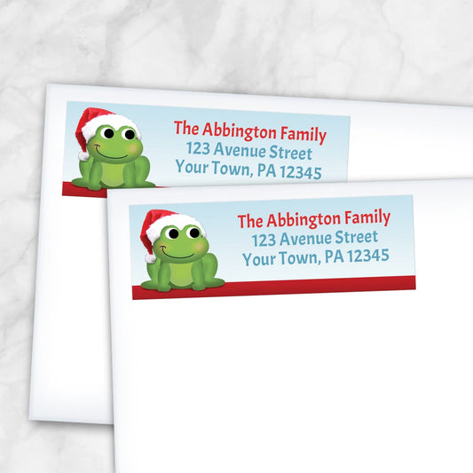 2 Santa Hat Frog Christmas Address Labels shown on white envelopes on a marble surface